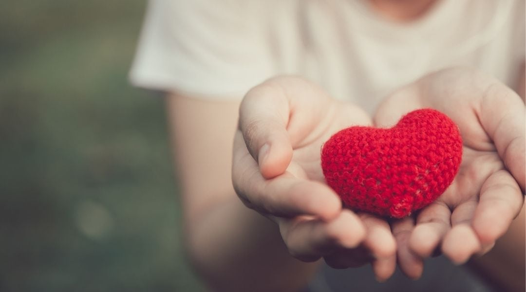 Woman's hands cupping a knitted heart - Share better core health with a friend